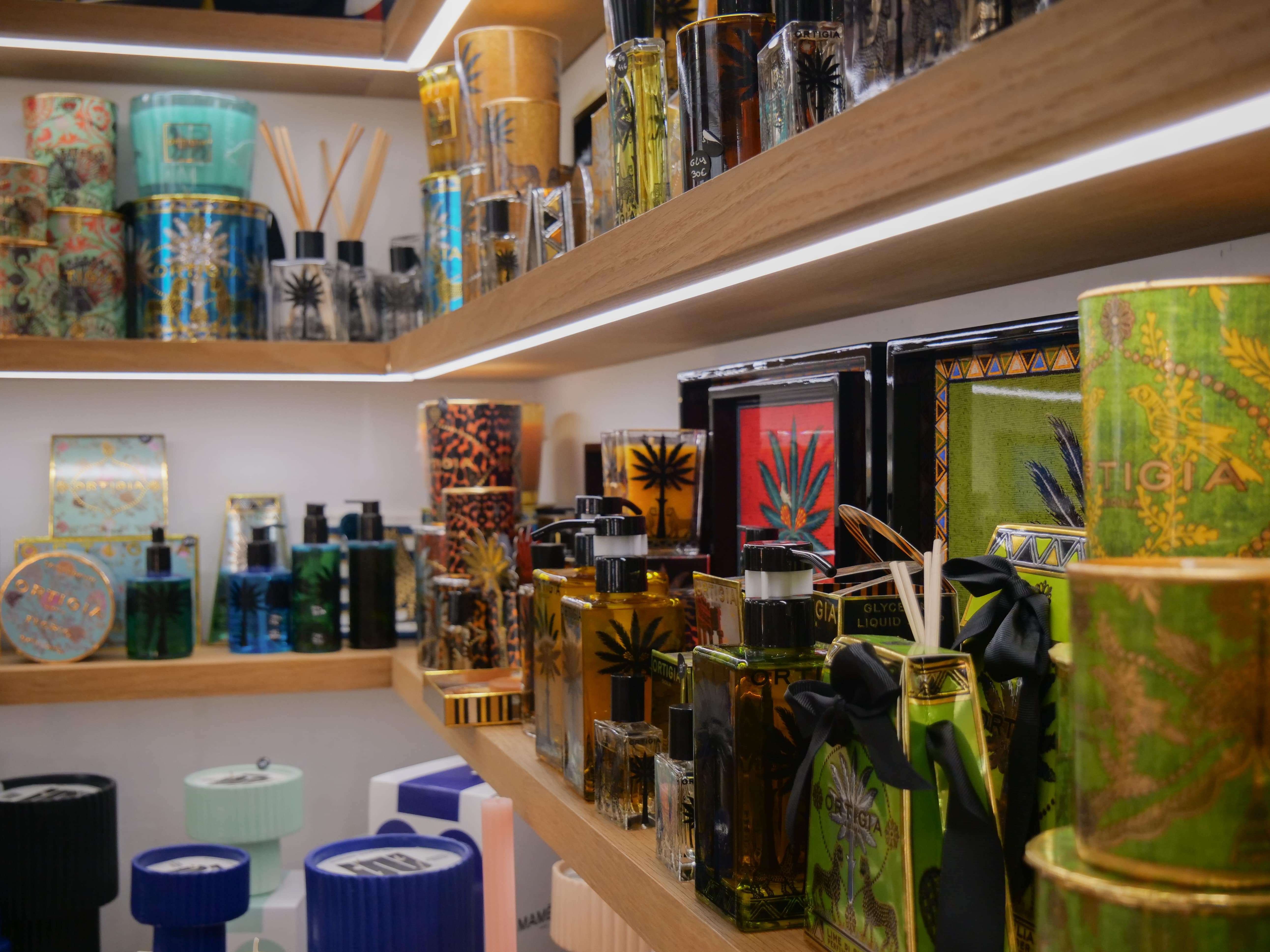 Produits de luxe Ortigia Sicilia sur des étagères en bois — bougies parfumées, diffuseurs, savons et parfums d’intérieur artisanaux italiens aux emballages colorés et raffinés, exposés dans une boutique haut de gamme.