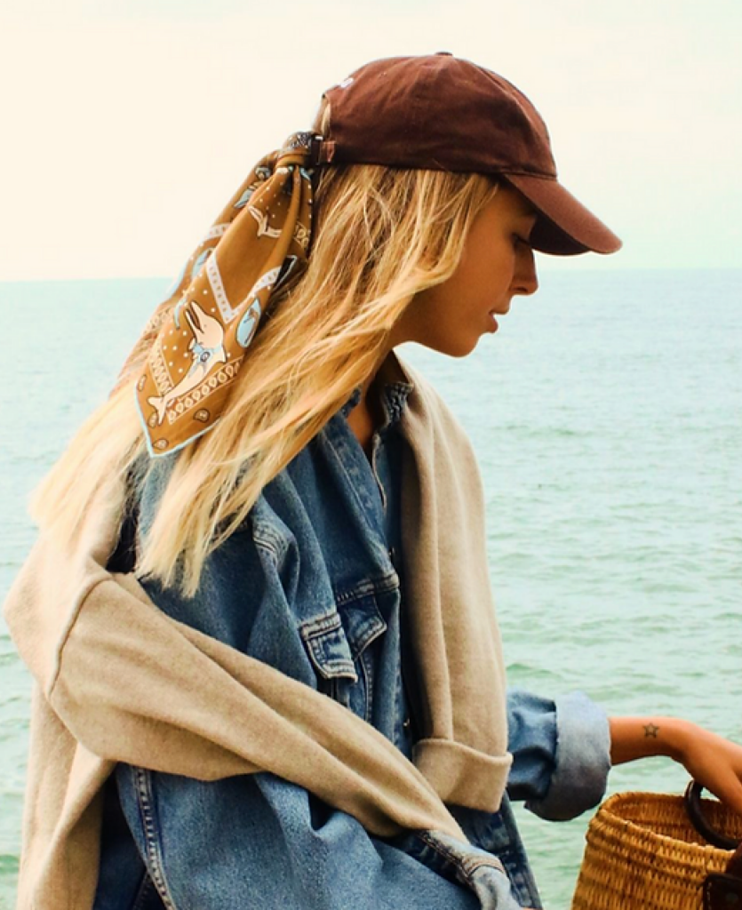 Femme portant un bandana en soie Soie-même noué à une casquette, face à l’océan, dans un univers inspiré de la Côte basque.
